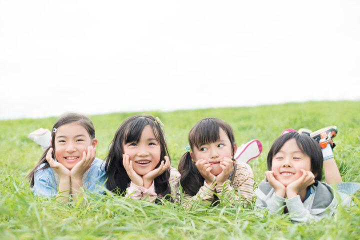 原っぱで寝転ぶ笑顔の子どもたち